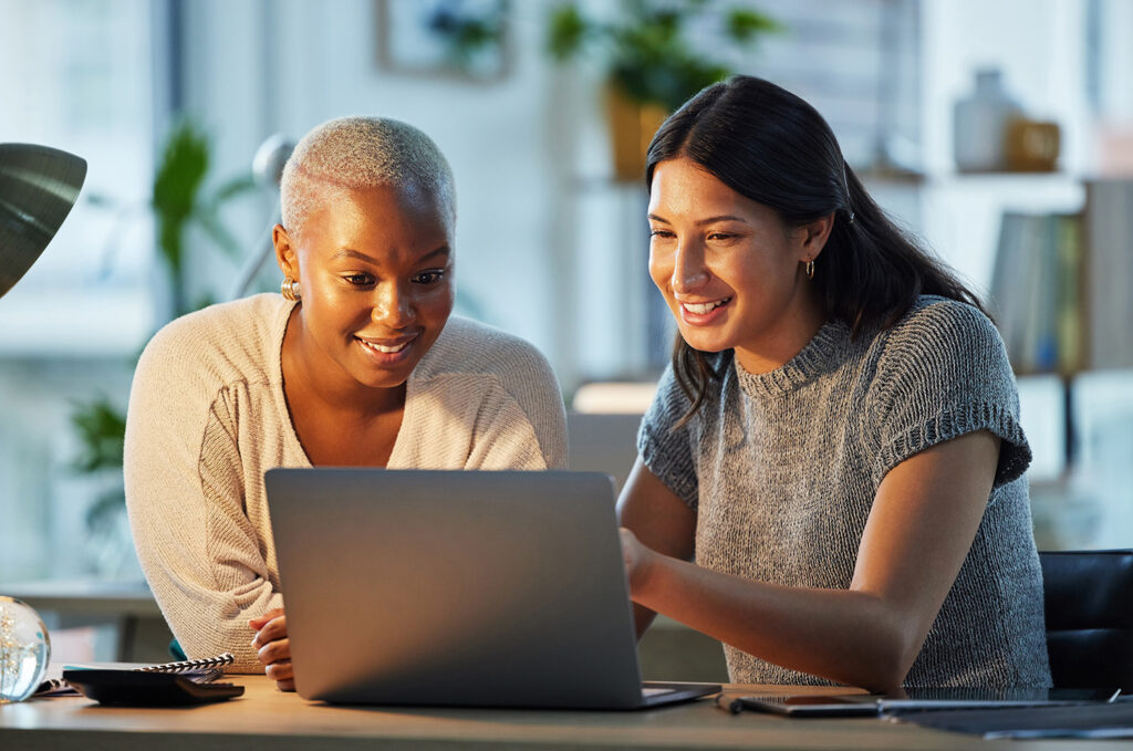 Two women looking at a laptop together while working on a project.